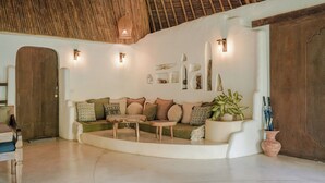 A cozy living room with a wooden ceiling, a sofa with patterned cushions, a coffee table, and a potted plant. - Mana Earthly Paradise (Ubud)