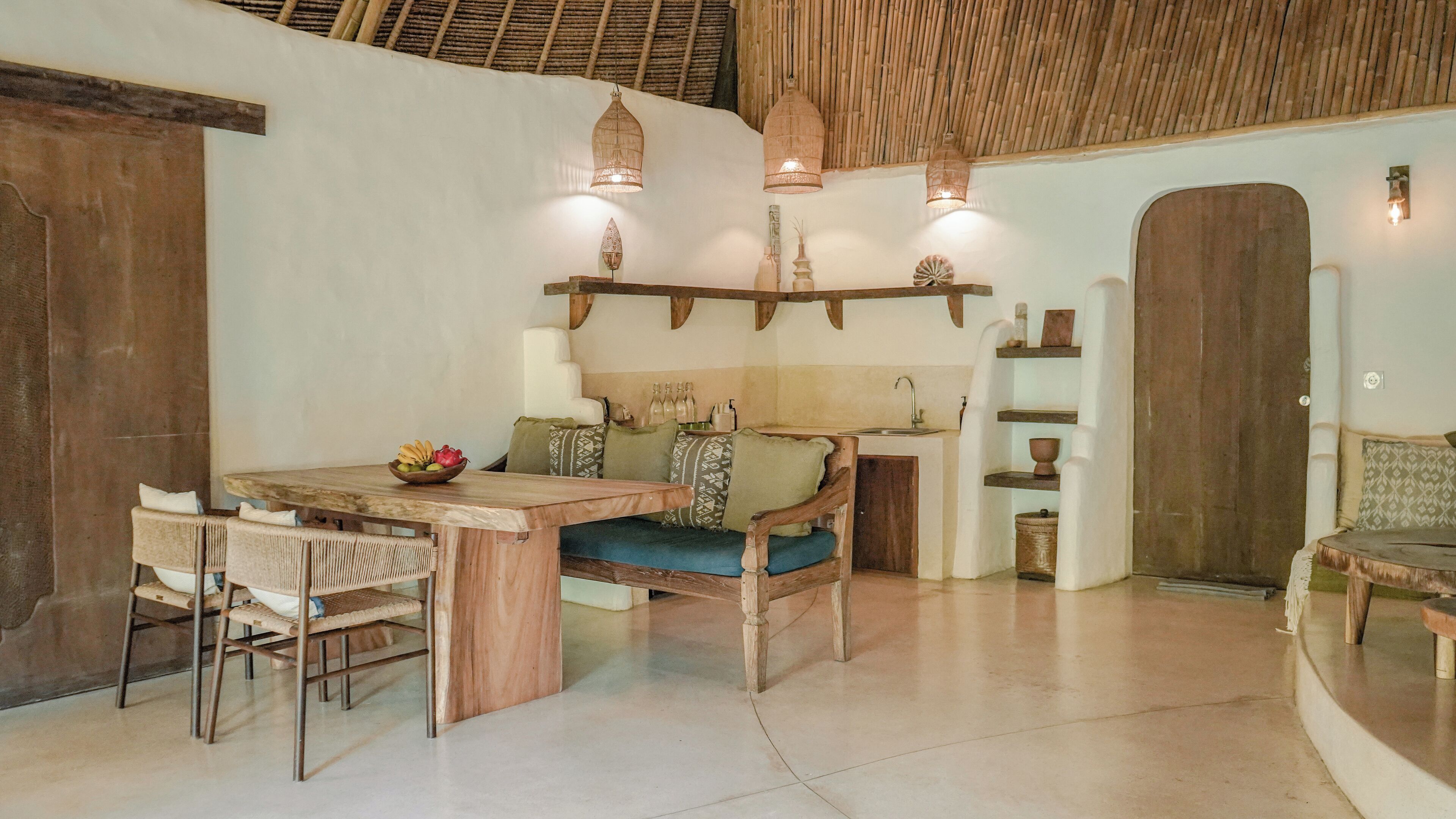 Un interior rústico con una mesa de comedor de madera, sillas, un sofá y una zona de cocina con un lavamanos y estanterías.