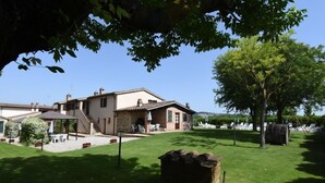 A two-story house with a patio area, outdoor seating, and a large tree. - Agriturismo Miralduolo (Torgiano)