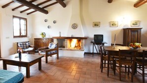 A cozy living room with a fireplace, wooden furniture, and a television. - Agriturismo Miralduolo (Torgiano)