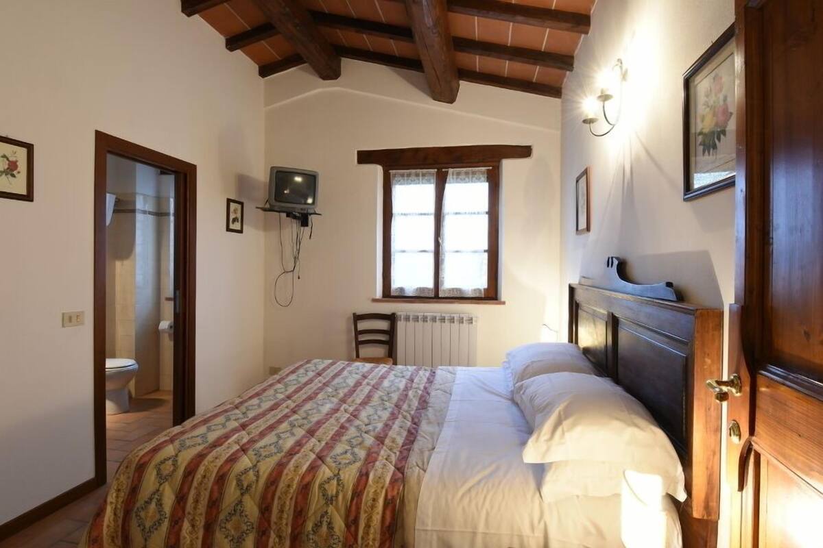 Een slaapkamer met een groot bed, een houten hoofdeinde, een aan de muur bevestigde televisie, een raam met gordijnen en een deur naar een andere kamer.