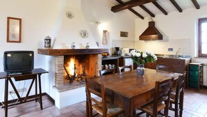 A rustic kitchen with a stone fireplace, wooden dining table, and a television on a small table. - Agriturismo Miralduolo (Torgiano)