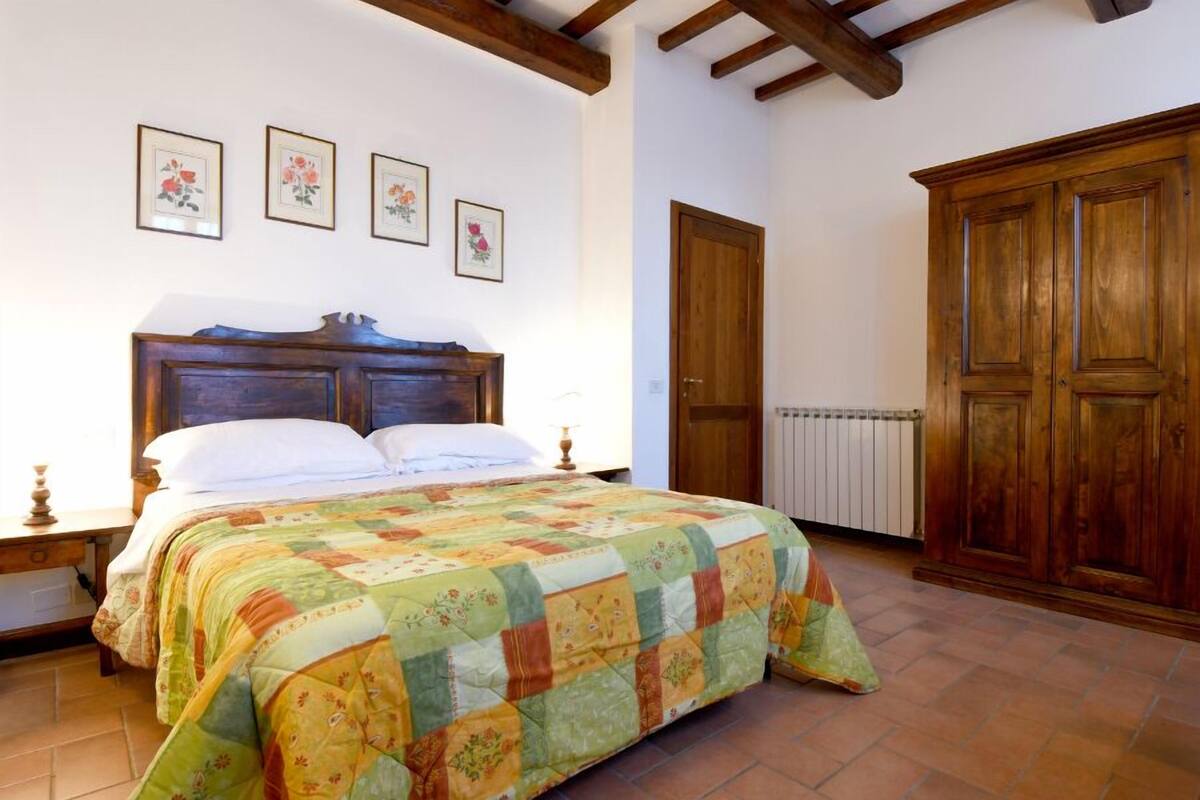 Een slaapkamer met een houten bed, een sprei, een houten kledingkast en een radiator.