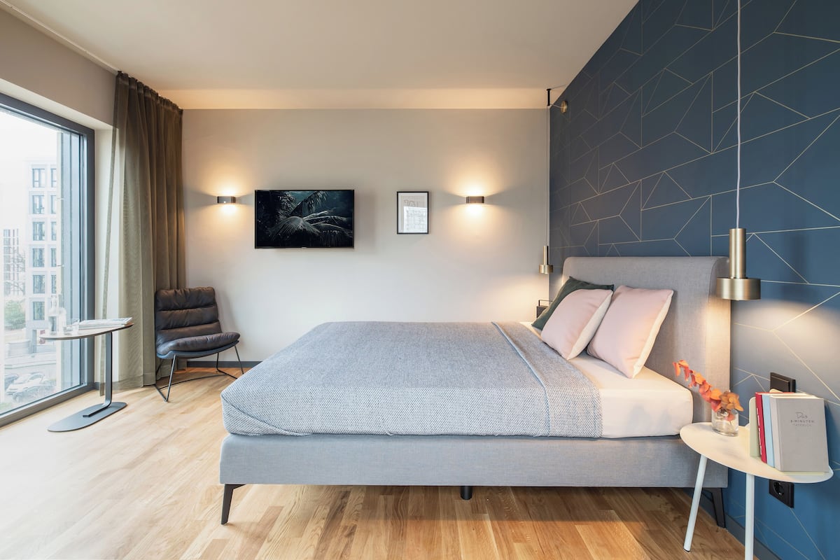 Une chambre moderne avec un grand lit, une table de chevet, une chaise et une vue sur la ville par la fenêtre.