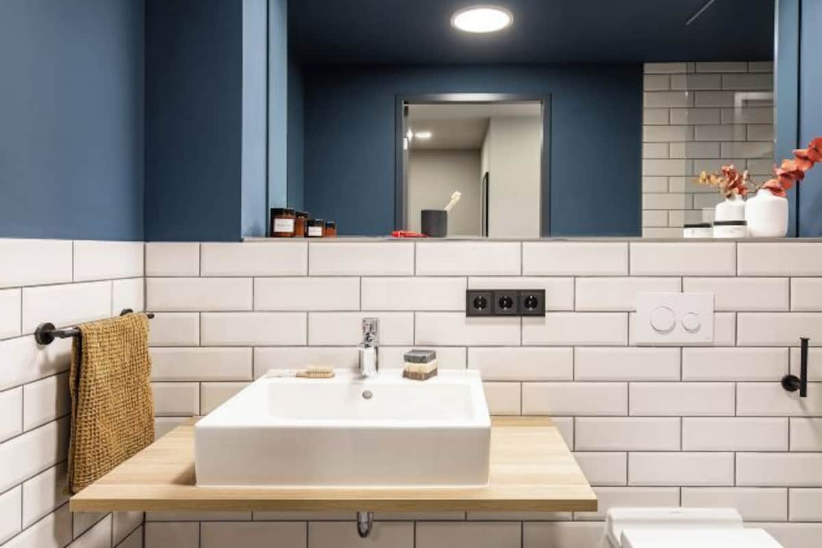 A bathroom with a white sink, wooden countertop, and a mirror above it. There are toiletries on the countertop and a towel hanging on the wall.