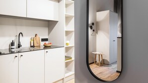 Een moderne keuken met witte kastjes, een zwart aanrecht en een spiegel die een eethoek met een kleine tafel en stoelen weerkaatst.