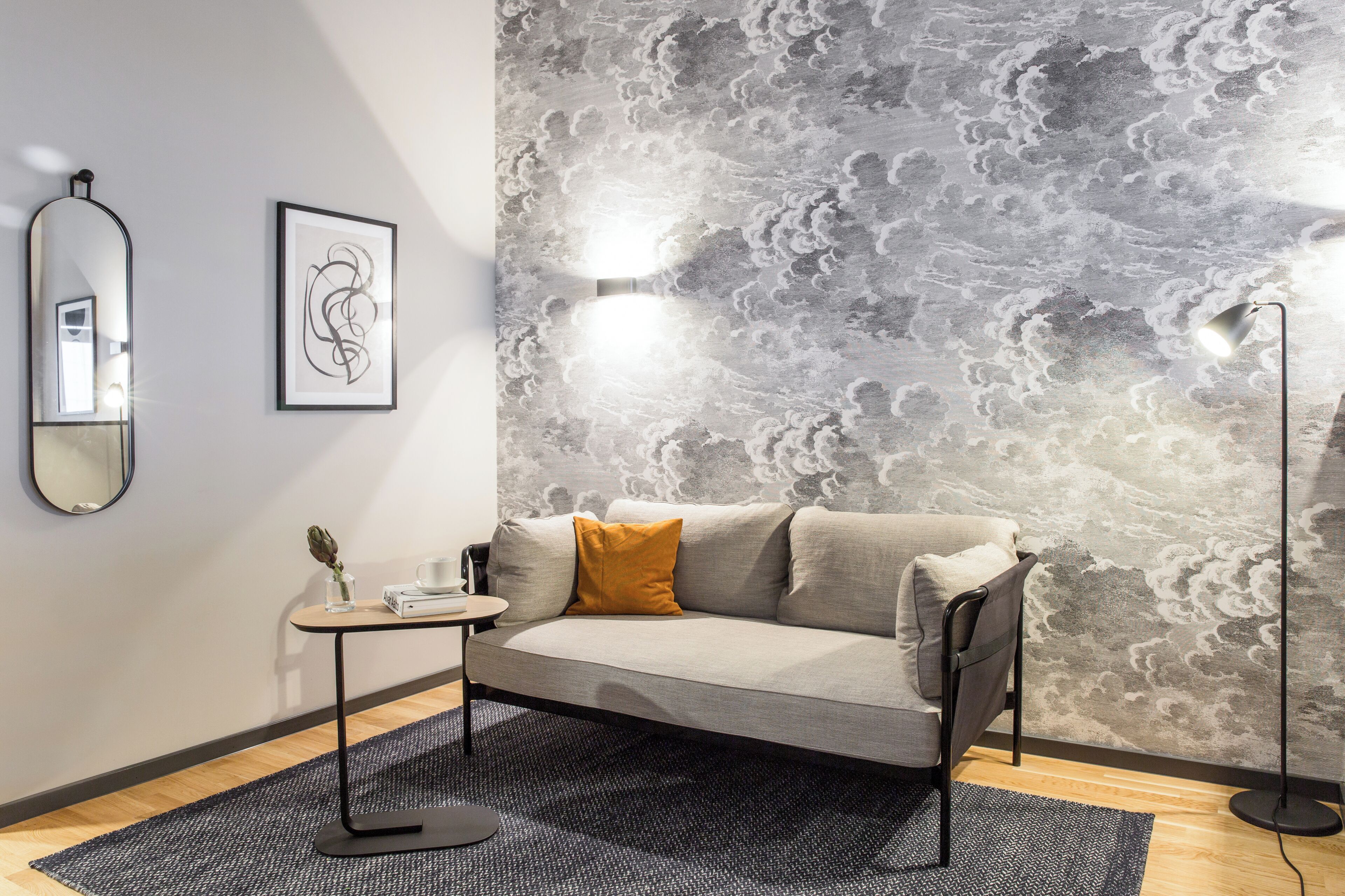 Ein modernes Wohnzimmer mit einem grauen Sofa, einem kleinen runden Tisch und einem dekorativen Spiegel.