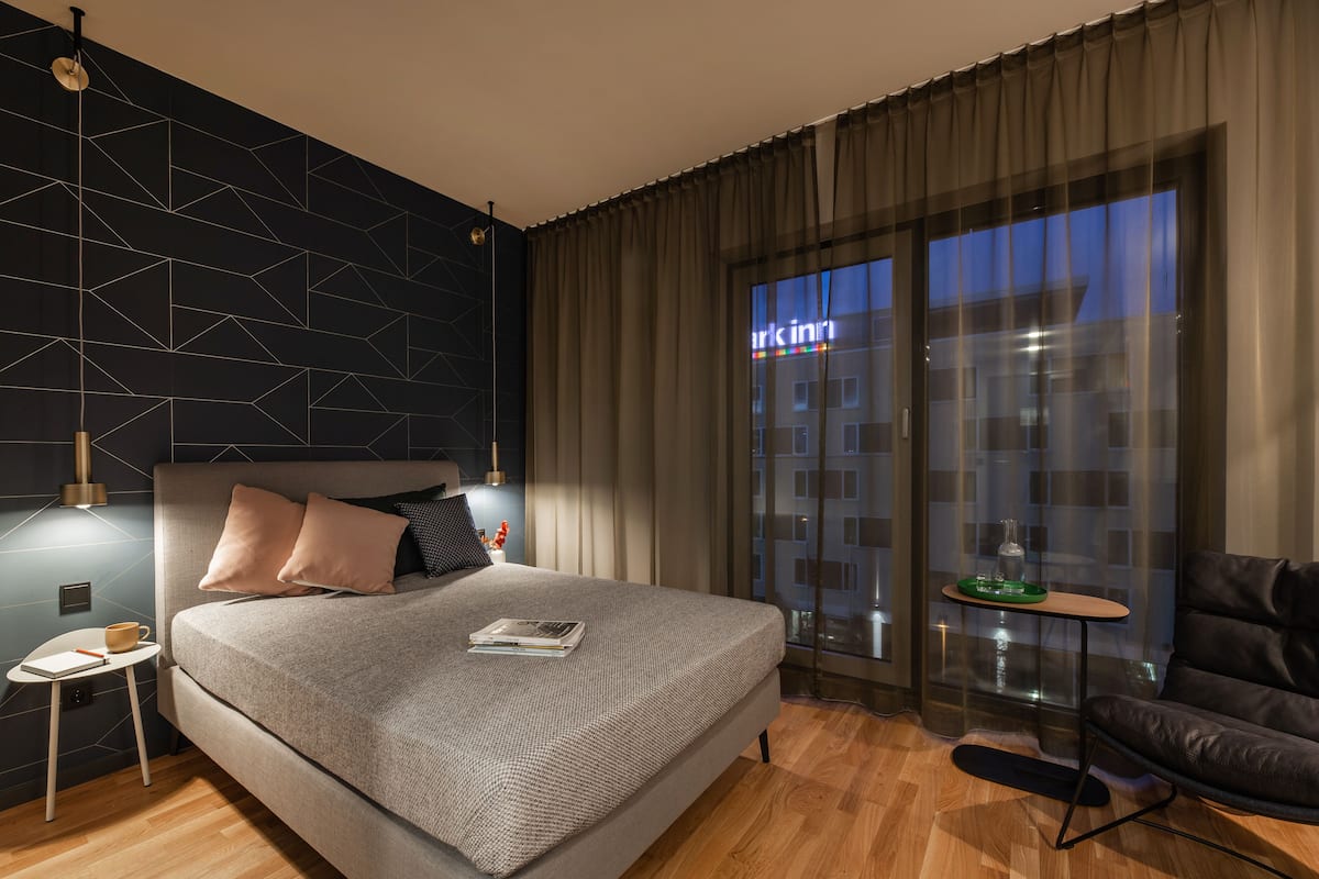 Une chambre à coucher moderne avec un grand lit, une table de chevet, une lampe de lecture, une table basse en verre et un fauteuil en cuir.