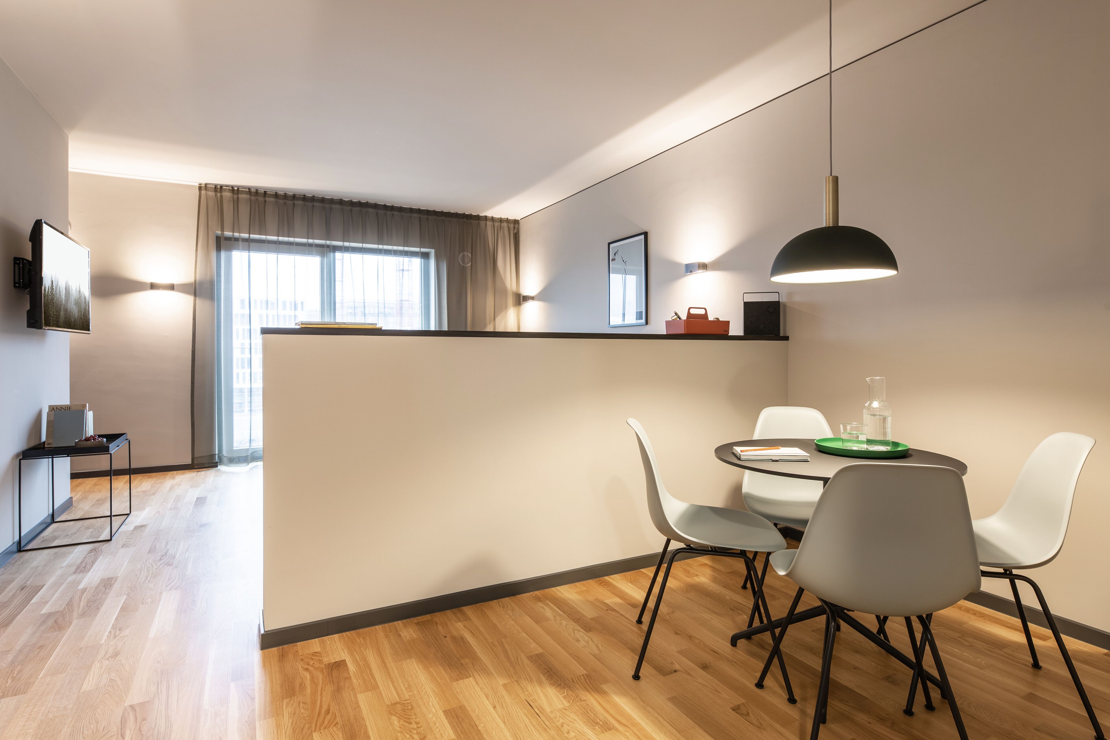 Un comedor moderno con una mesa redonda, sillas blancas y una lámpara colgante.