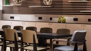 Een moderne eetruimte met een lange tafel en stoelen, een wand van houten latten, hangende bolvormige lampen en groene decoratieve vazen.