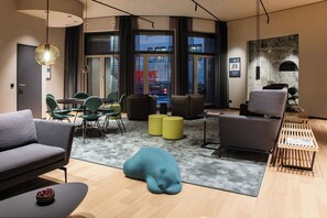 Eine moderne Hotellobby mit einer Couch, Sesseln, einem Tisch, einem Couchtisch und einem großen Fenster mit Vorhängen.