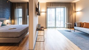 Een moderne hotelkamer met een bed, een bank, een kleine tafel en een aan de muur bevestigde televisie.