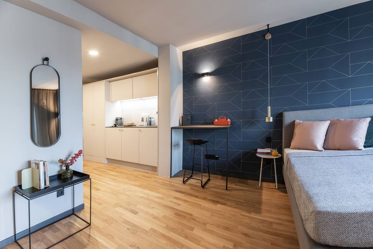 Une chambre moderne avec un grand lit, un petit bureau et, au fond, un coin cuisine.