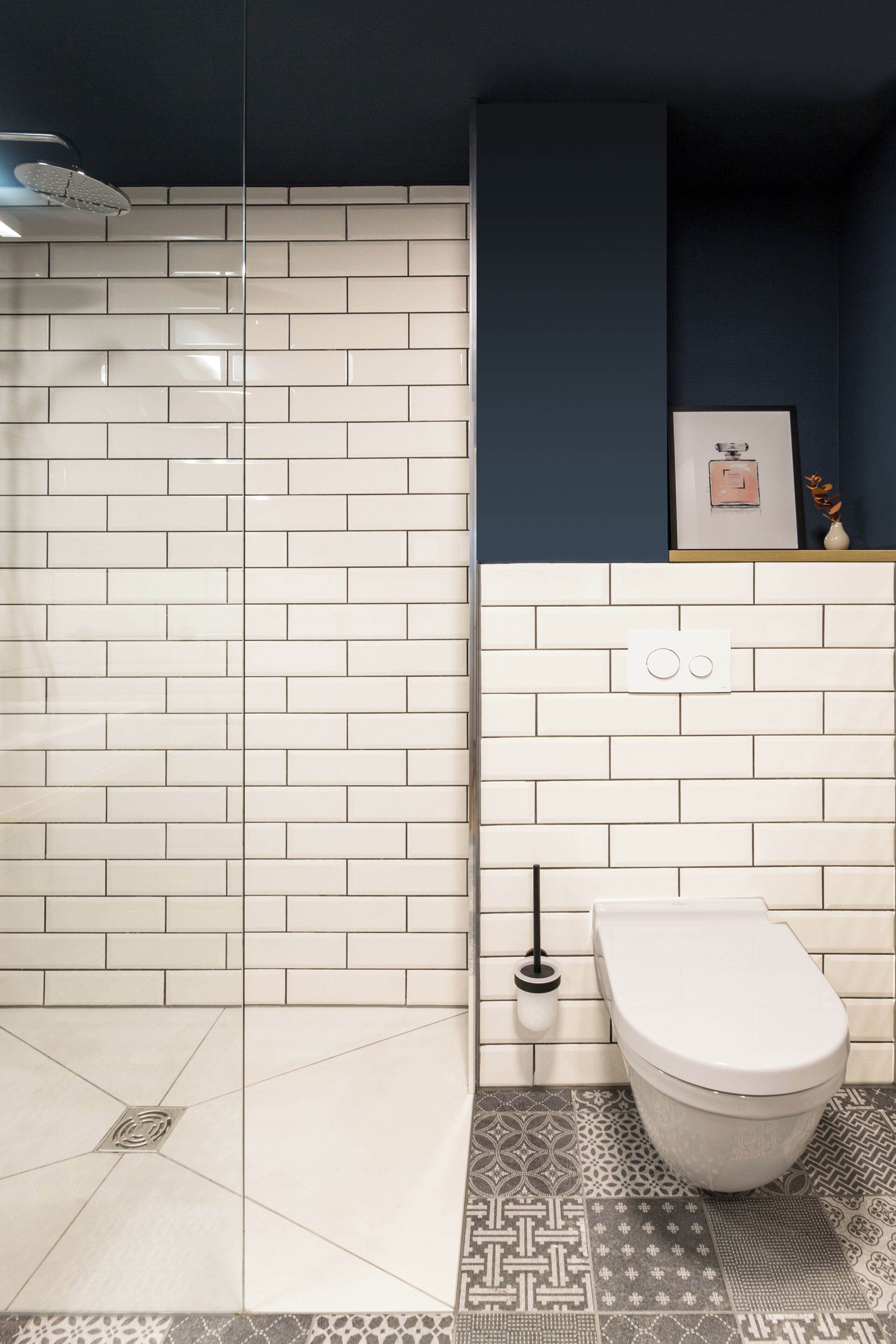 A bathroom with white subway tiles, a shower, a toilet, and patterned floor tiles.