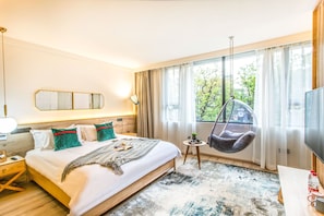 A modern hotel room with a large bed, a hanging chair, a small table with a bottle and mug, and a TV on a wooden stand. - Suzhou BuerJu (Suzhou)