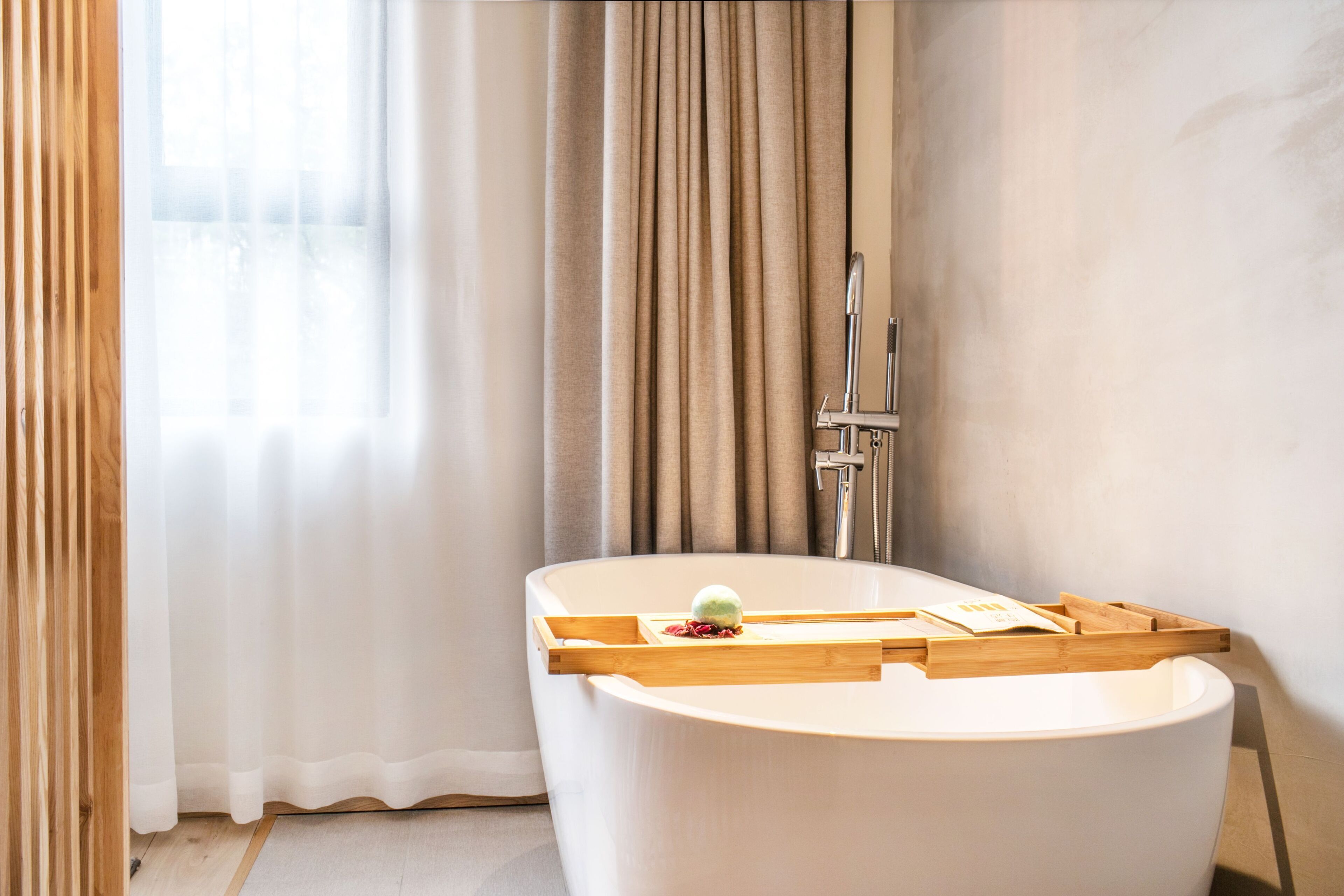 A modern bathroom with a freestanding bathtub, wooden tray, and a green bath mat.