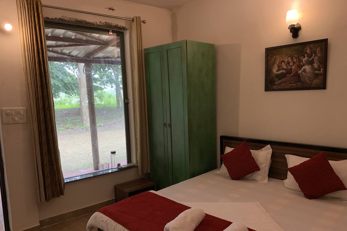 Quarto de hotel com cama, guarda-roupa verde, um quadro na parede e uma janela com cortinas.
