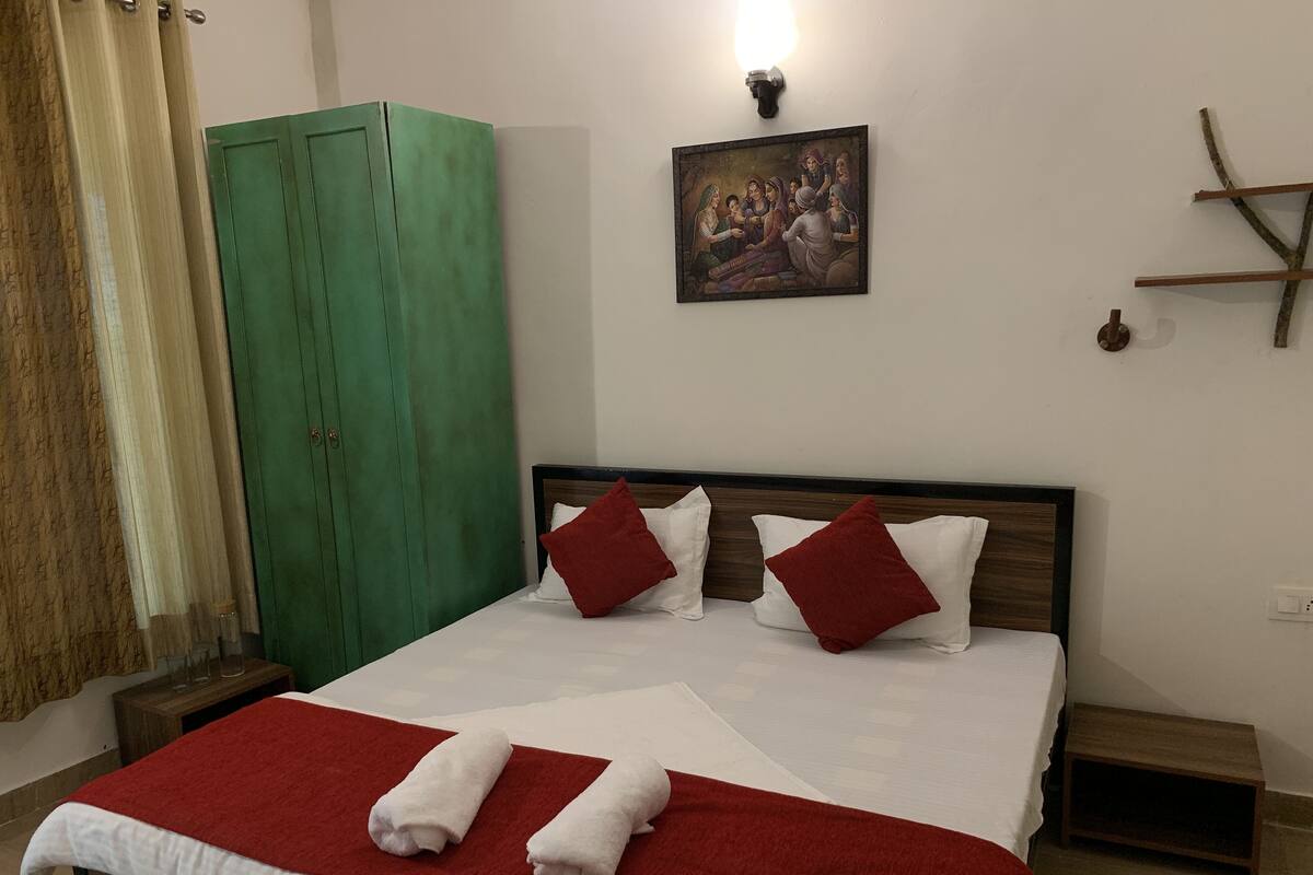 Uma cama bem arrumada com almofadas vermelhas e brancas, um guarda-roupa verde e um quadro pendurado na parede.