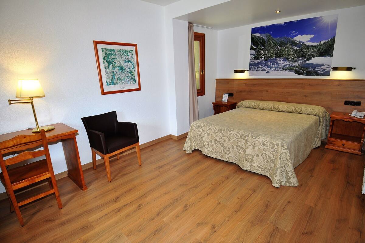 Ein Hotelzimmer mit Bett, Schreibtisch, Stuhl, Lampe und einem Bild an der Wand.