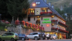 Ein Hotel mit mehreren Balkonen, die mit Blumen geschmückt sind, einer Steinfassade und Blick auf eine Berglandschaft.