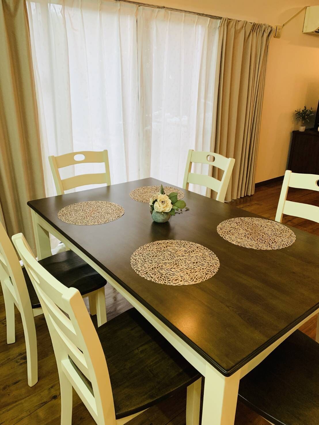 A dining table with four chairs, a vase with flowers, and a decorative doily on each chair's seat.