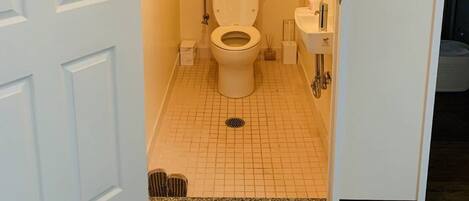 A small, narrow bathroom with a toilet, sink, and shower.