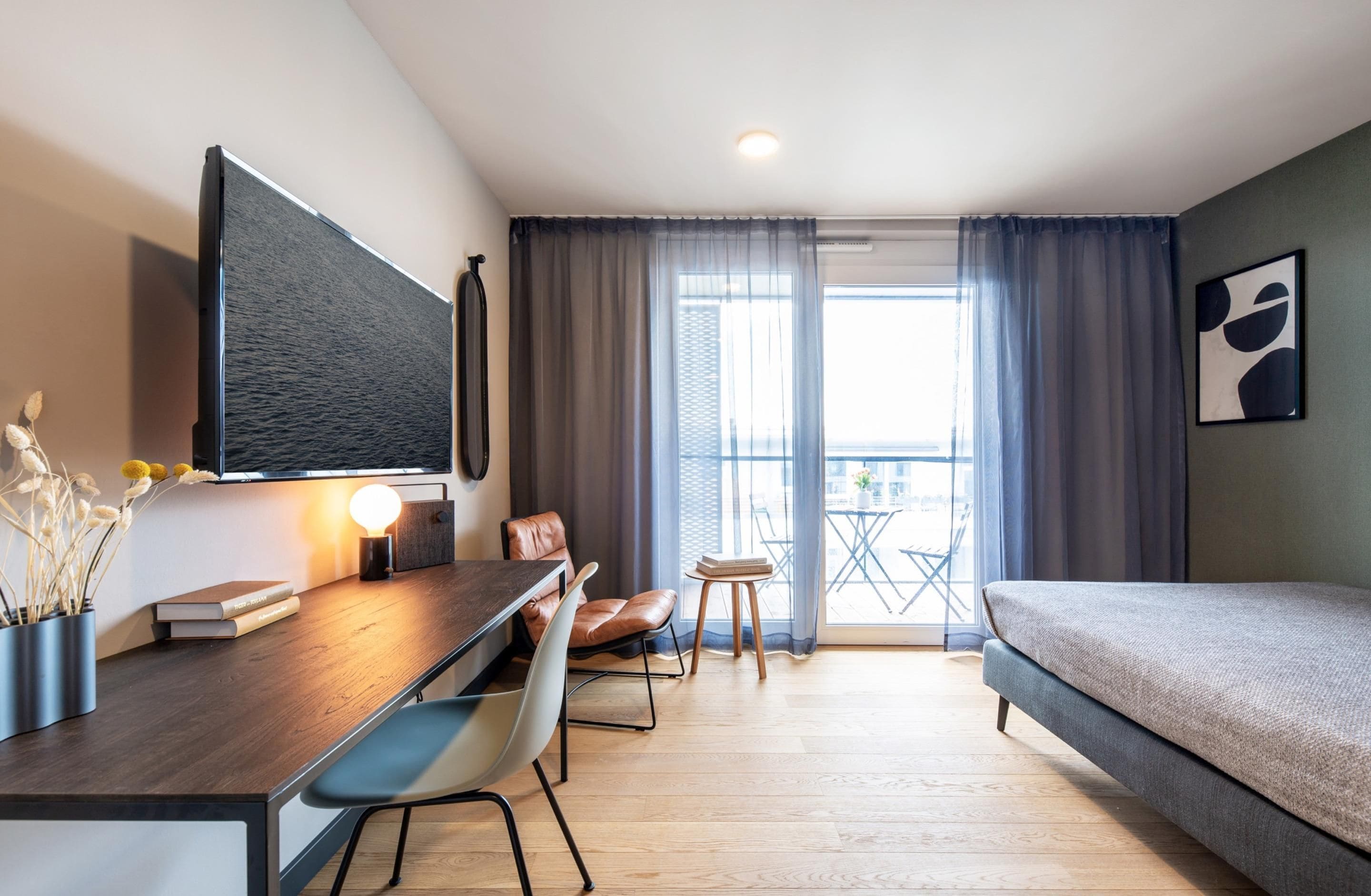 Une chambre d’hôtel moderne équipée d’un lit, d’un bureau avec une chaise, d’une télévision, d’une petite table et d’un balcon avec vue.
