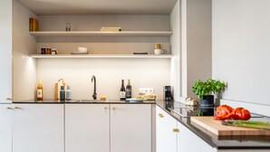A modern kitchen with white cabinets, a black countertop, and a built-in stove. There are shelves above the counter holding books and jars. - ipartment Boeblingen @HOME by Best Western (Boeblingen)