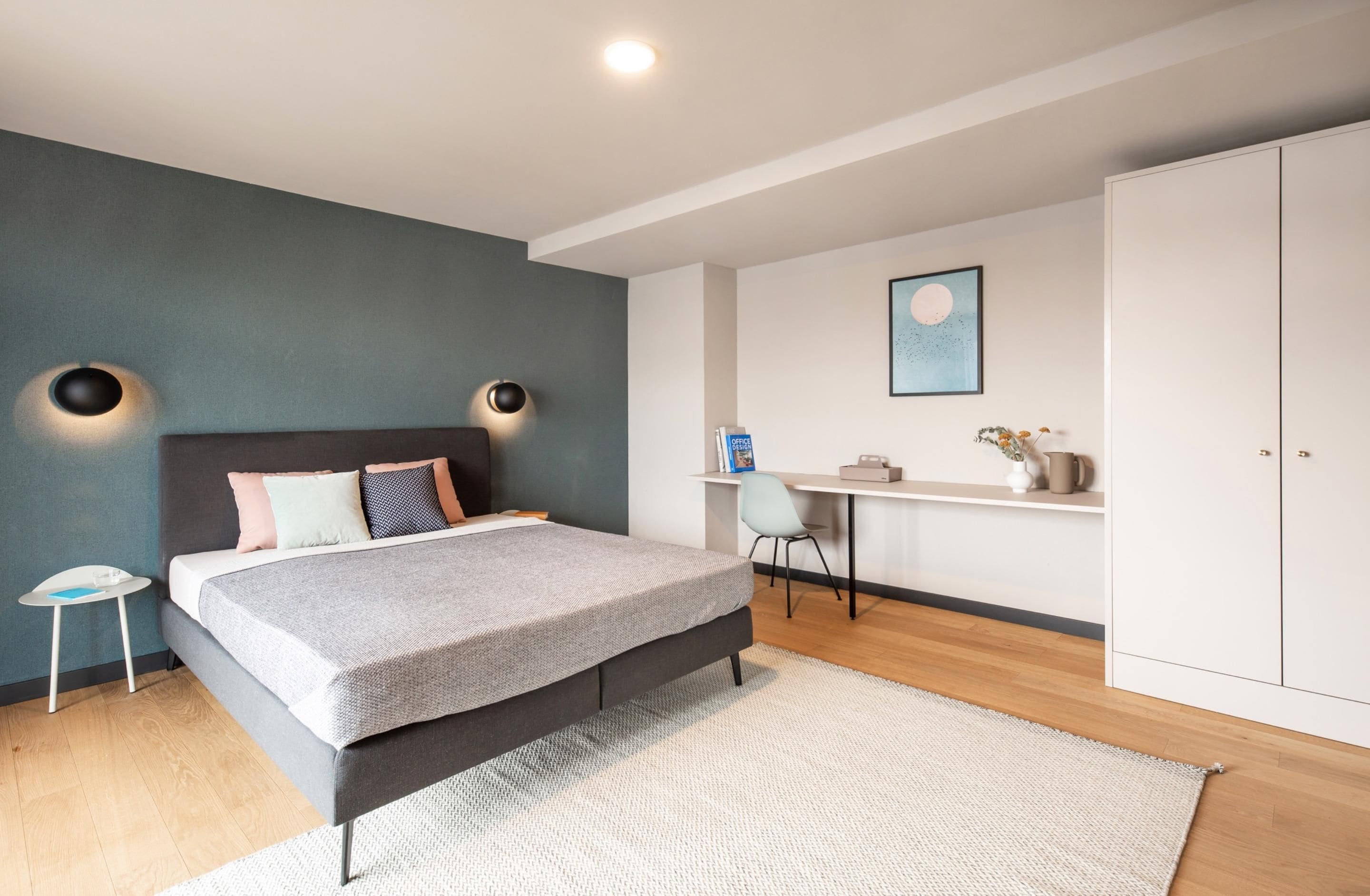 A modern bedroom with a bed, bedside tables, a desk, and a wardrobe.