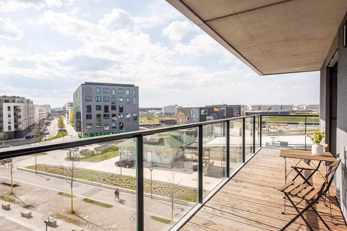 Ein Balkon mit Blick auf eine Stadtlandschaft, darunter moderne Gebäude und eine Straße.