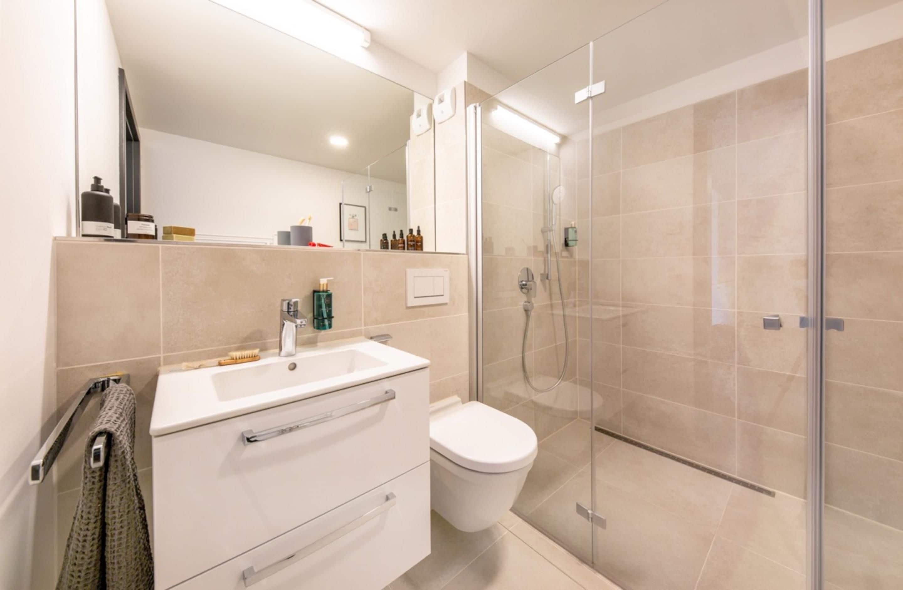 Un baño moderno con cabina de ducha de vidrio, un lavabo blanco y un inodoro.