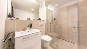 Un baño moderno con cabina de ducha de vidrio, un lavabo blanco y un inodoro.