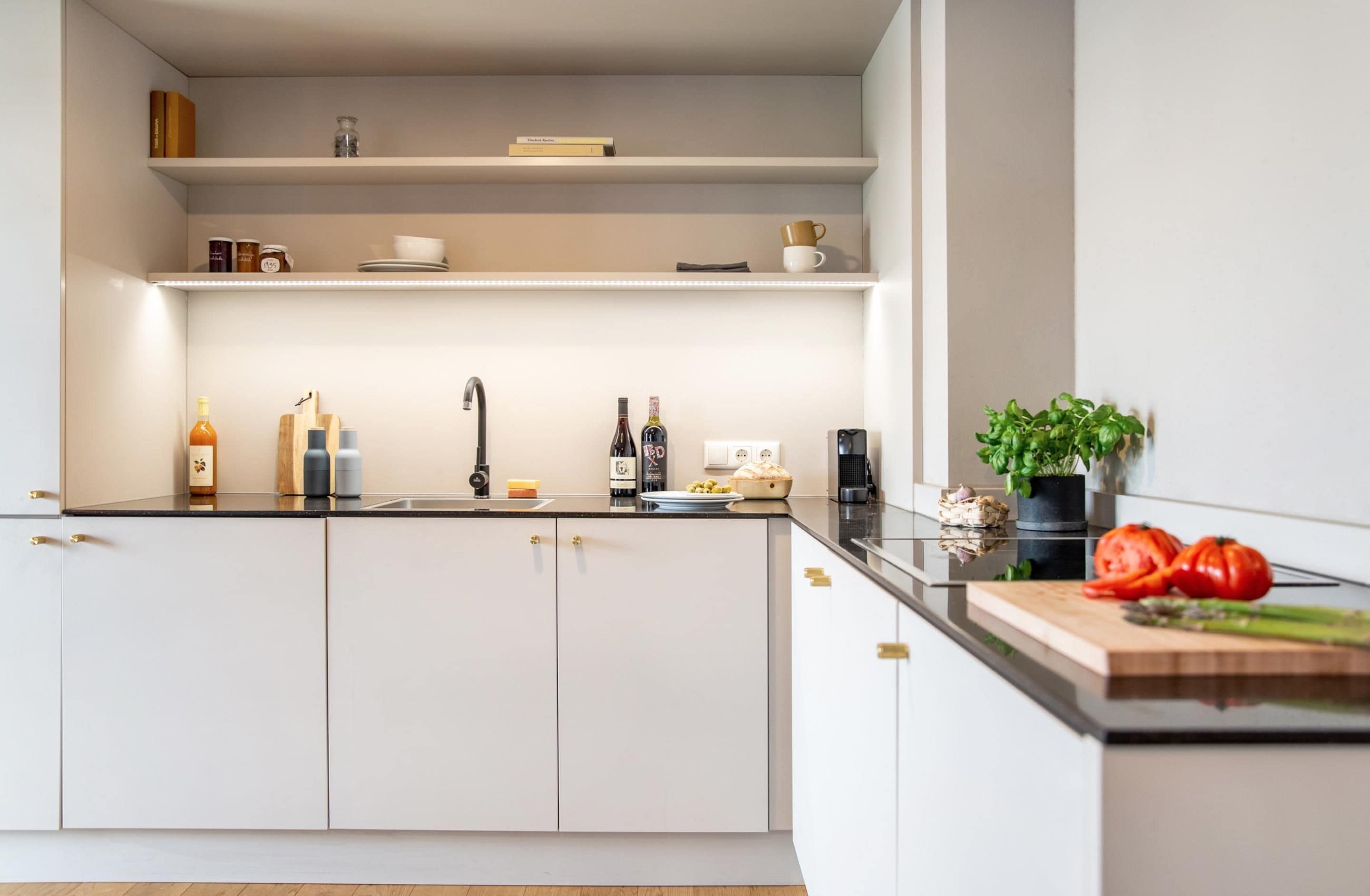 Una cocina moderna con armarios blancos, una encimera negra y una tabla de cortar de madera con verduras.