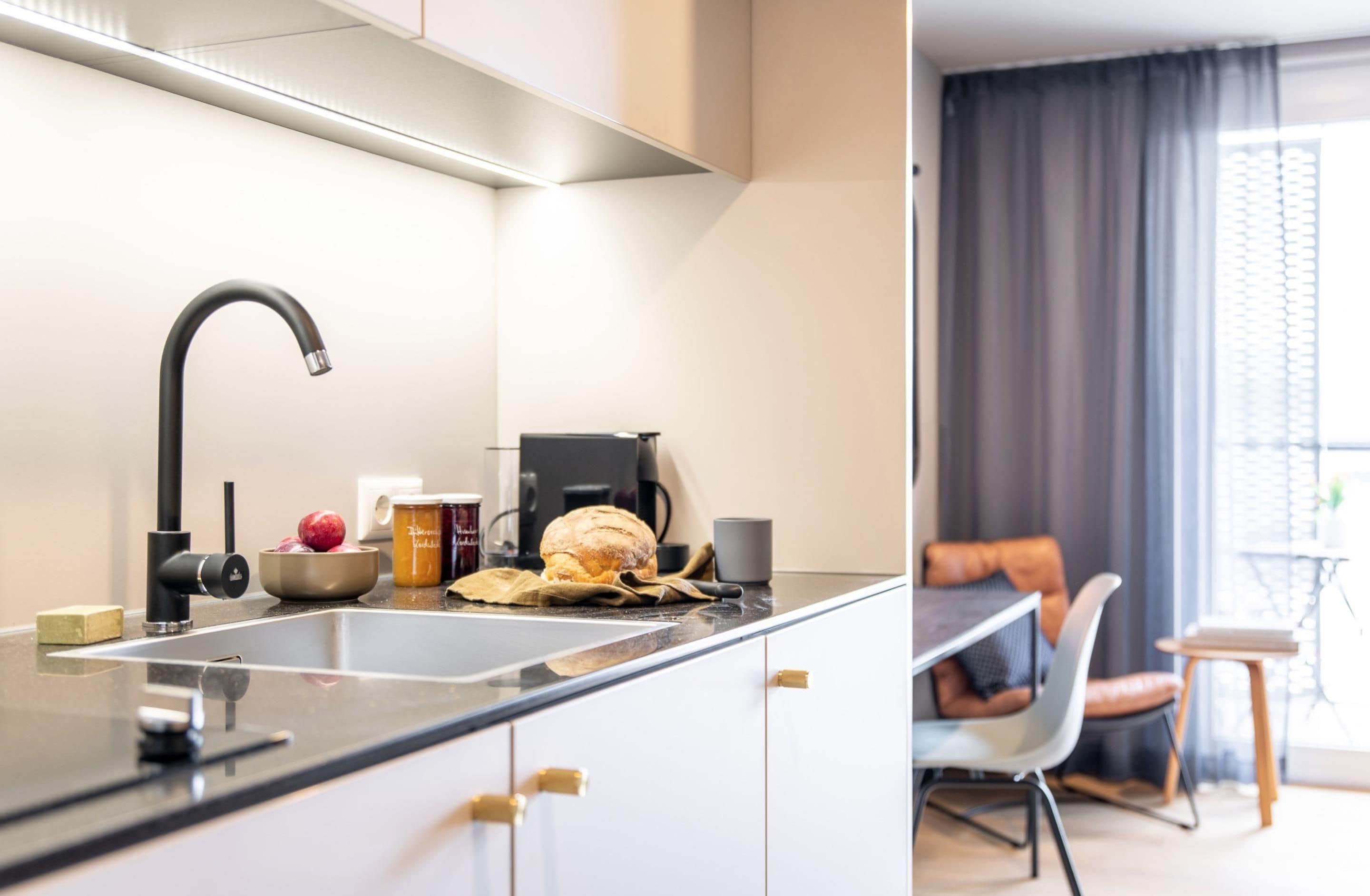 Una cocina moderna con un grifo negro, una cafetera y una zona de comedor con mesa y sillas.