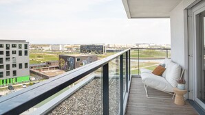 A balcony with a white sofa, a small table with a plant, and a view of a cityscape with buildings and a sports field. - ipartment Boeblingen @HOME by Best Western (Boeblingen)