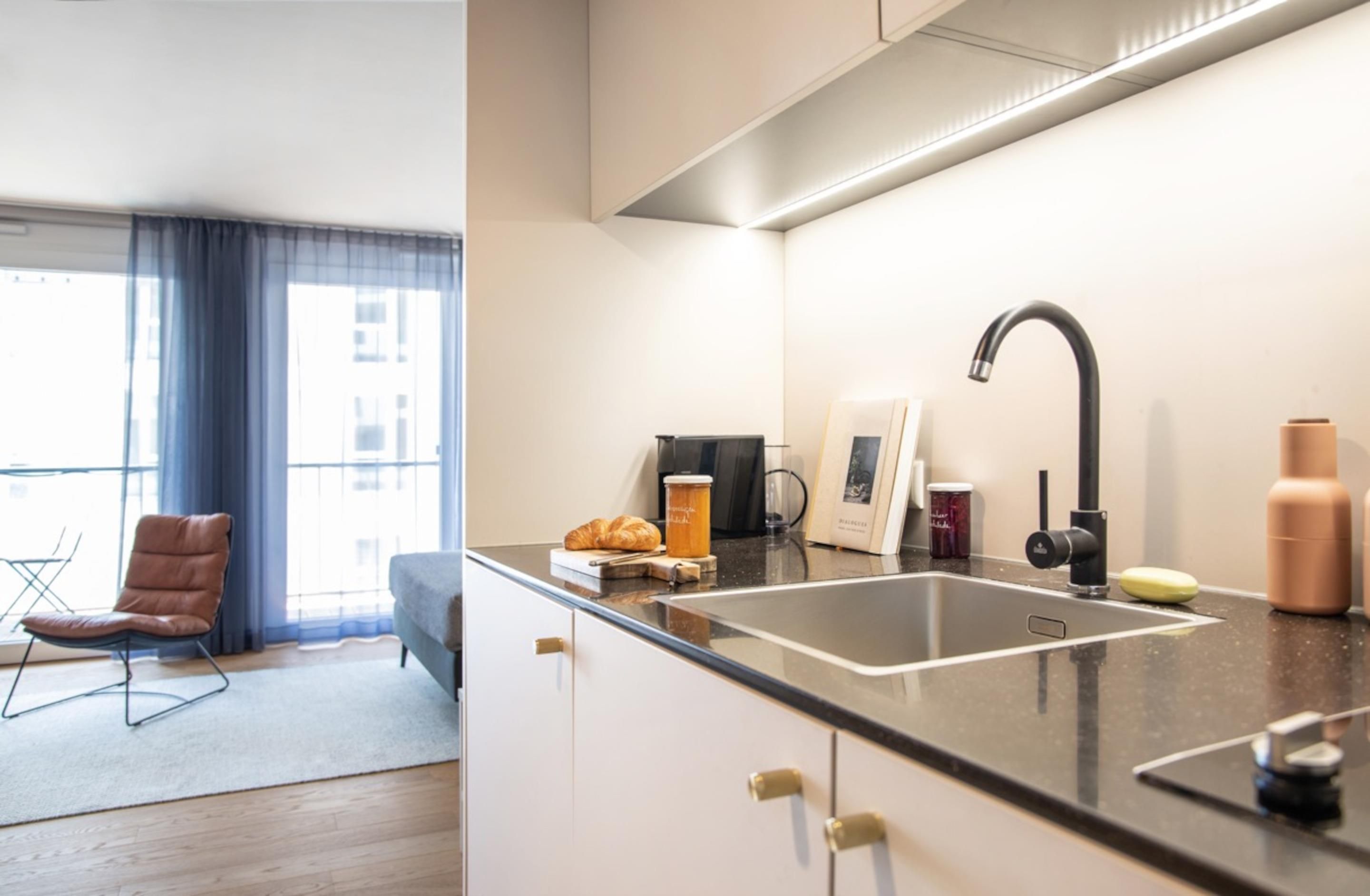 A modern kitchen with a black countertop, stainless steel sink, and a coffee machine.
