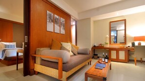 Ein Hotelzimmer mit einer Couch, einem Holztischchen, einem Schreibtisch mit Spiegel und einem Bett mit blauen und weißen Kissen.