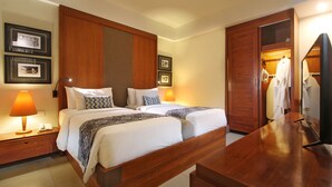 Ein Hotelzimmer mit zwei Betten, einem Holzkopfstück, Nachttischen mit Lampen, einem Schreibtisch aus Holz und einem Kleiderschrank.