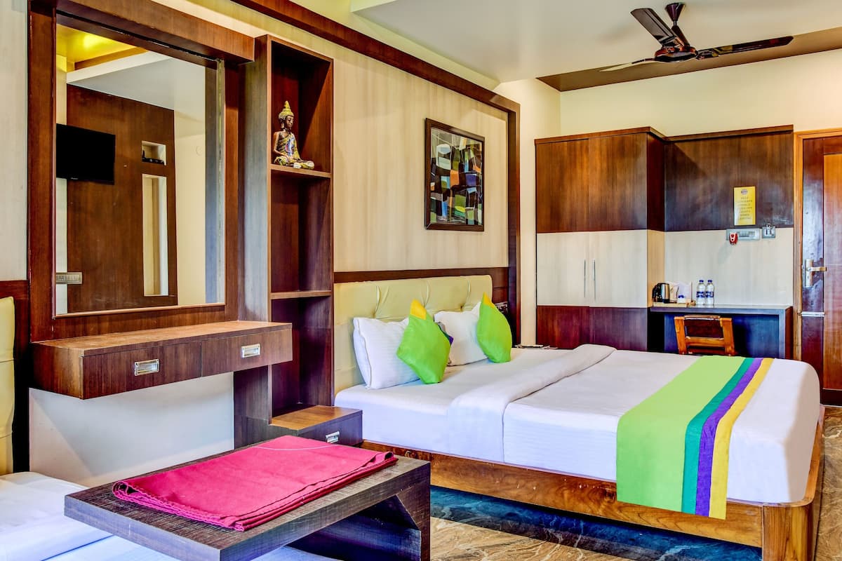 A hotel room with a bed, bedside table, a mirror, a wardrobe, a desk with a chair, and a ceiling fan.