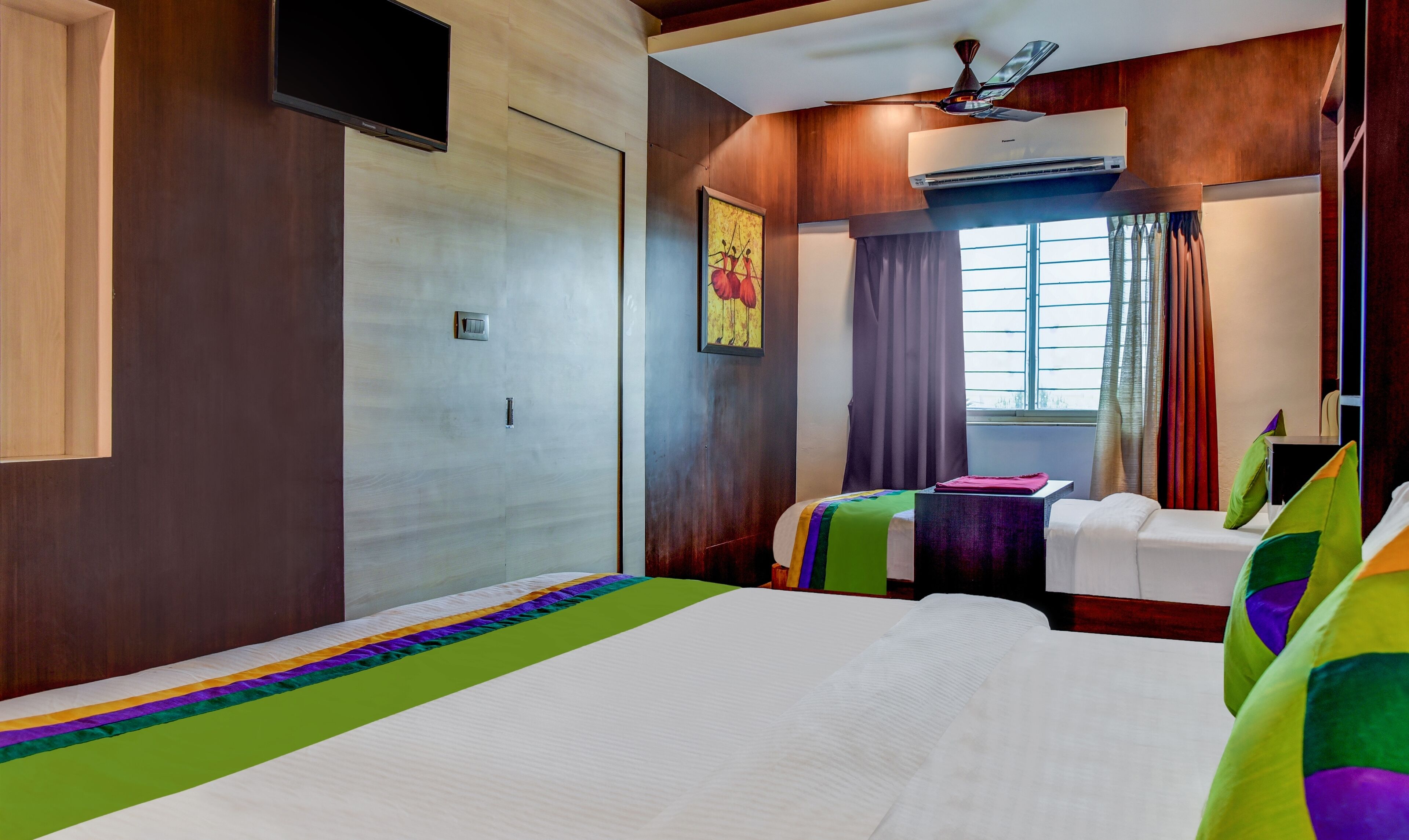 A hotel room with a large bed, a TV, an air conditioning unit, and a window with curtains.