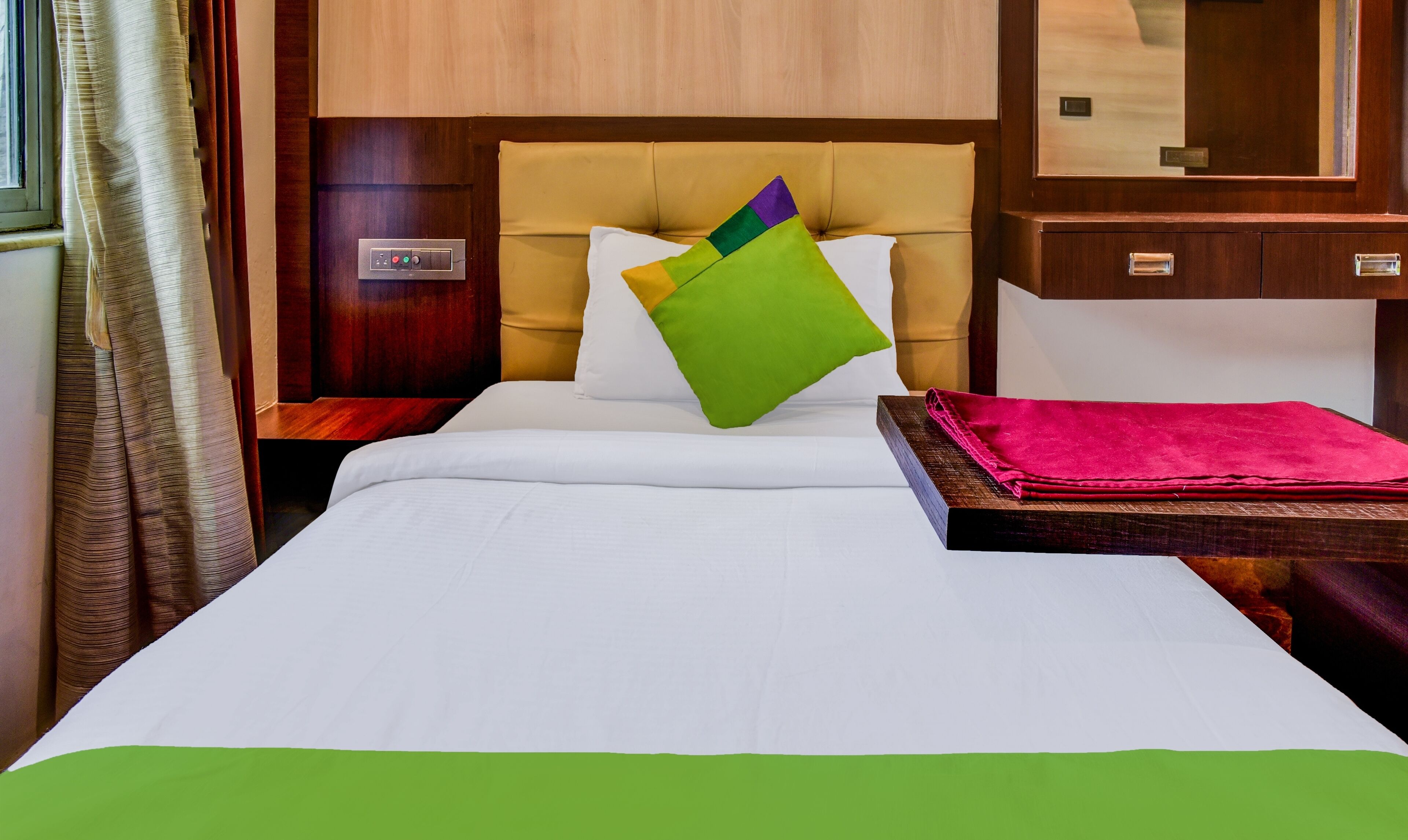 A hotel room with a bed, a wooden headboard, a bedside table with a red cloth, and a wooden nightstand.