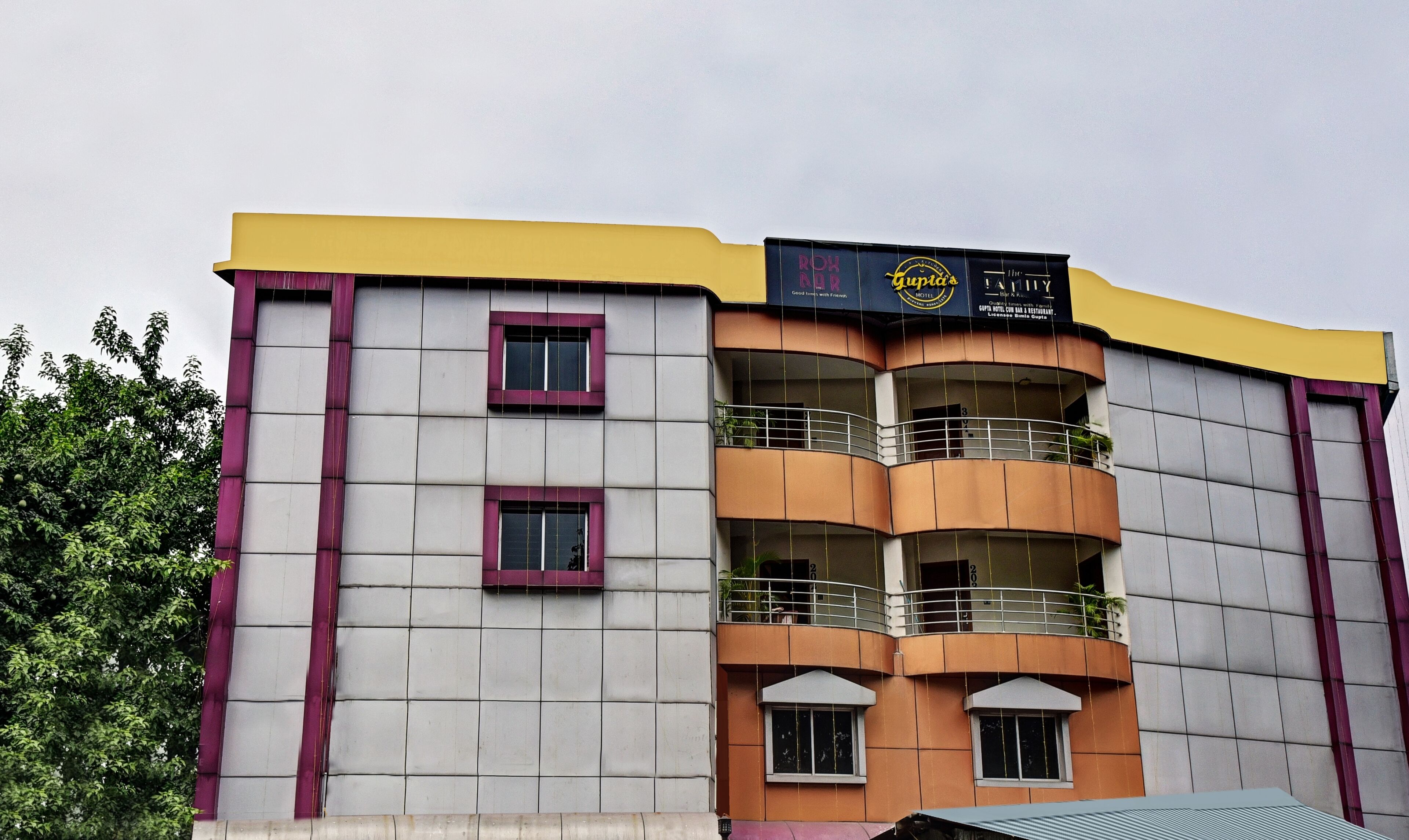 A multi-story building with a yellow and purple facade, balconies, and a sign for 'Roh Ado Hotel'.