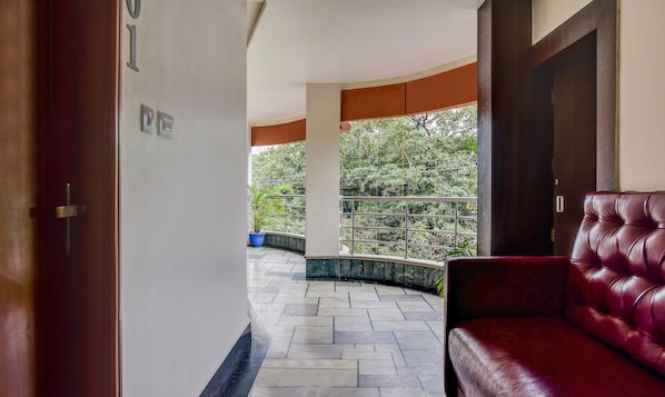 A corridor with a red leather sofa, a tiled floor, and a balcony with a railing.