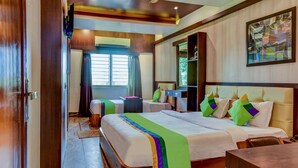Habitación de hotel con una cama grande, una cama más pequeña, un escritorio y una silla. Cuenta con una ventana con cortinas, un cuadro en la pared y una puerta.