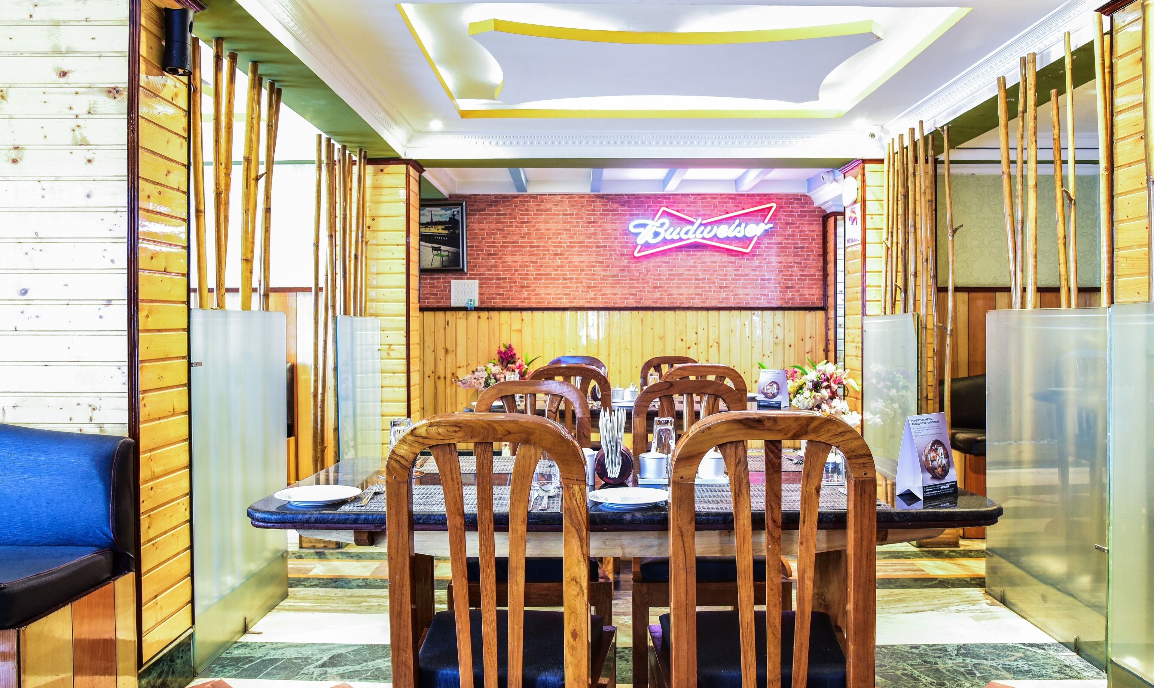Un restaurante con paredes de madera y un letrero de neón. Las mesas están dispuestas con sillas y tienen menús y vasos.