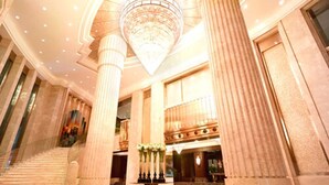 A grand lobby with high ceilings, large columns, and a central chandelier.