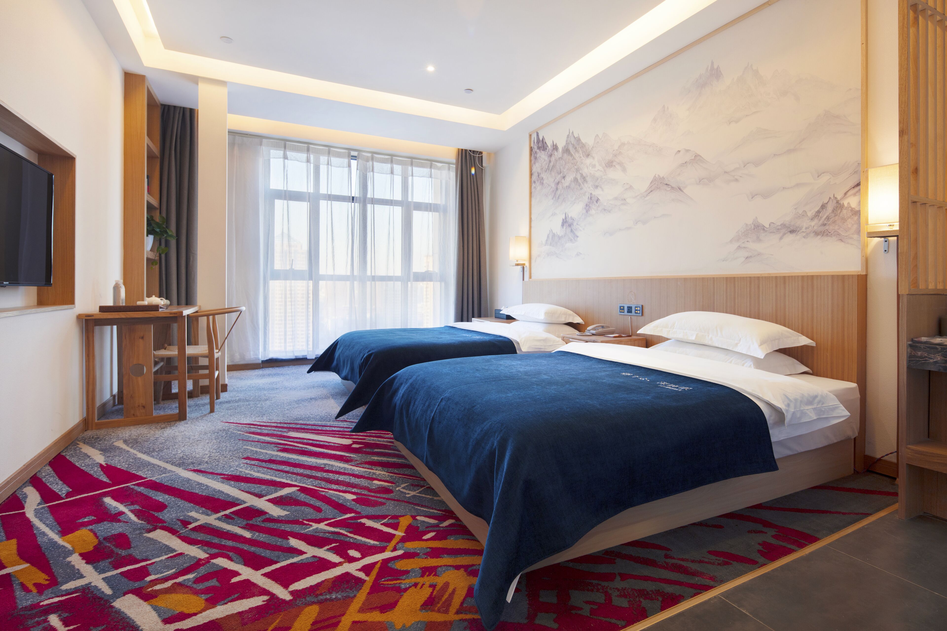 A hotel room with two beds, a large window, a mounted TV, and a painting on the wall.