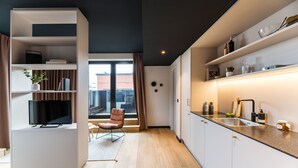 A modern kitchen with a built-in TV, wooden flooring, and a view of the city through large windows.
