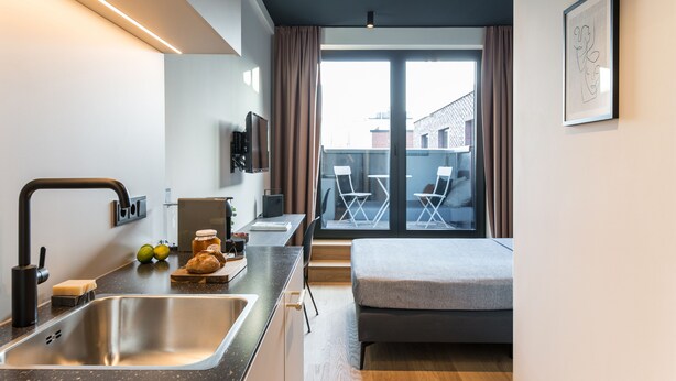 A modern kitchen with a sink, countertop, and a dining area with chairs.