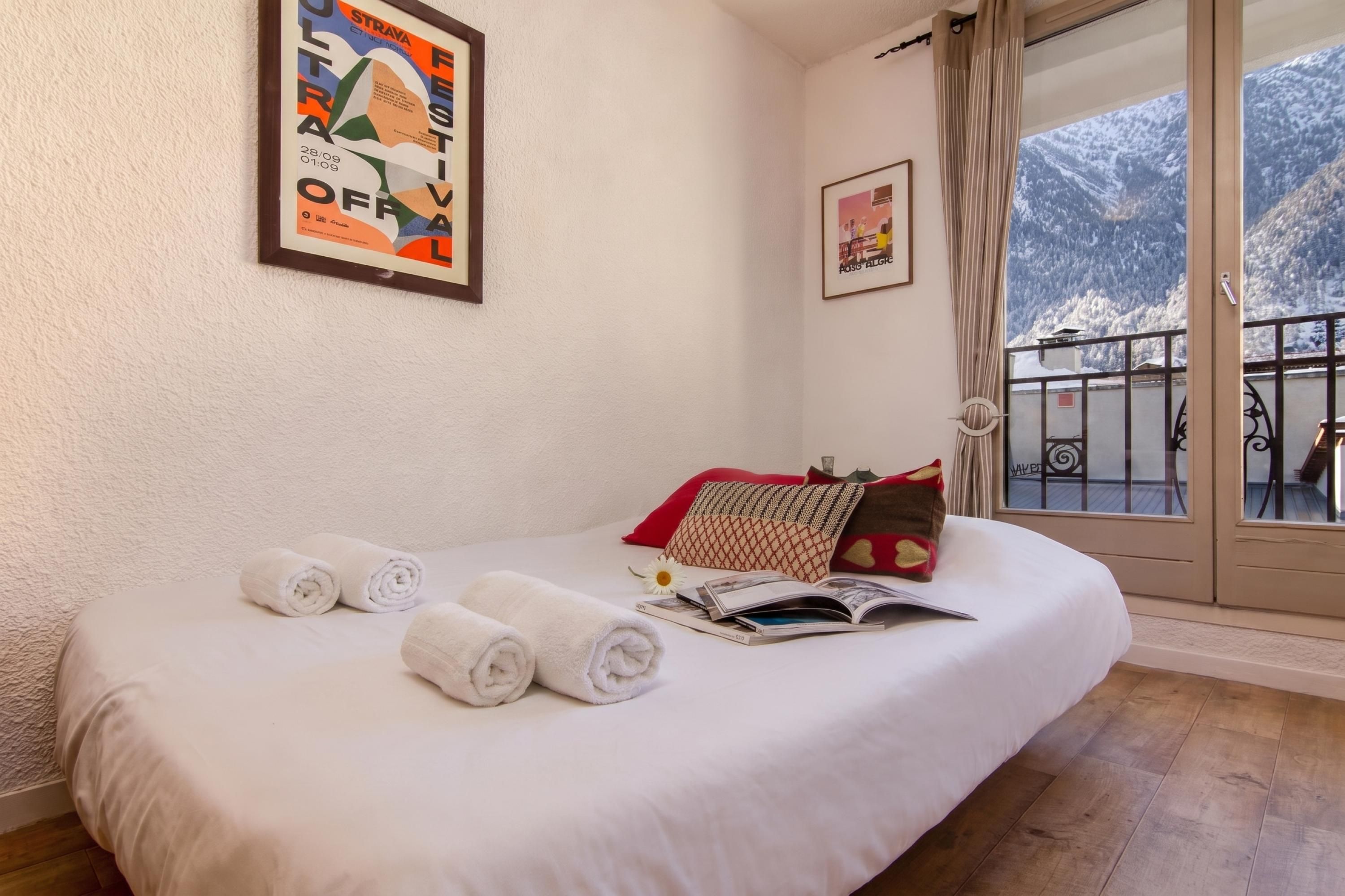 A hotel room with a bed, towels, a window with a mountain view, and a framed poster on the wall.